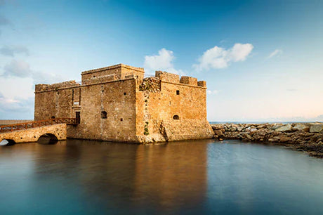 Castle on Cyprus coast with rock formations, ocean view, and serene lake in foreground