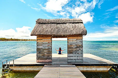 Wooden hut on Mauritius coast with thatched roof, overlooking serene ocean and cloudy sky