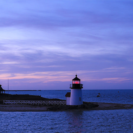 Nantucket lighthouse at dusk with glowing beacon and purple sky over calm ocean – coastal New England wall art for serene home or nautical office décor.