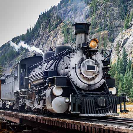 Train wall art featuring a vintage black steam locomotive on mountain tracks with pine trees and rocky cliffs — Train Wall Art Collection for travel and industrial decor.