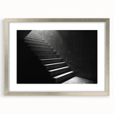 Textured art print of an abstract staircase in muted gray tones on a framed silver mat, suitable for bedroom decor.
