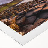 Art deco poster depicting the rugged coastline of Northern Ireland in muted green and blue tones on rolled canvas.
