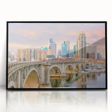 Large abstract wall art depicting the Minneapolis skyline in muted blue and gray tones, presented in a black framed acrylic.