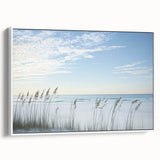 Framed canvas artwork depicting a serene beach landscape with gentle waves and a clear sky, featuring a crisp white frame that enhances its coastal aesthetic.
