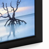 Framed canvas artwork depicting a serene beach landscape at sunset, showcasing vibrant colors of orange, pink, and blue with soft waves lapping at the shore. Perfect for coastal decor enthusiasts.
