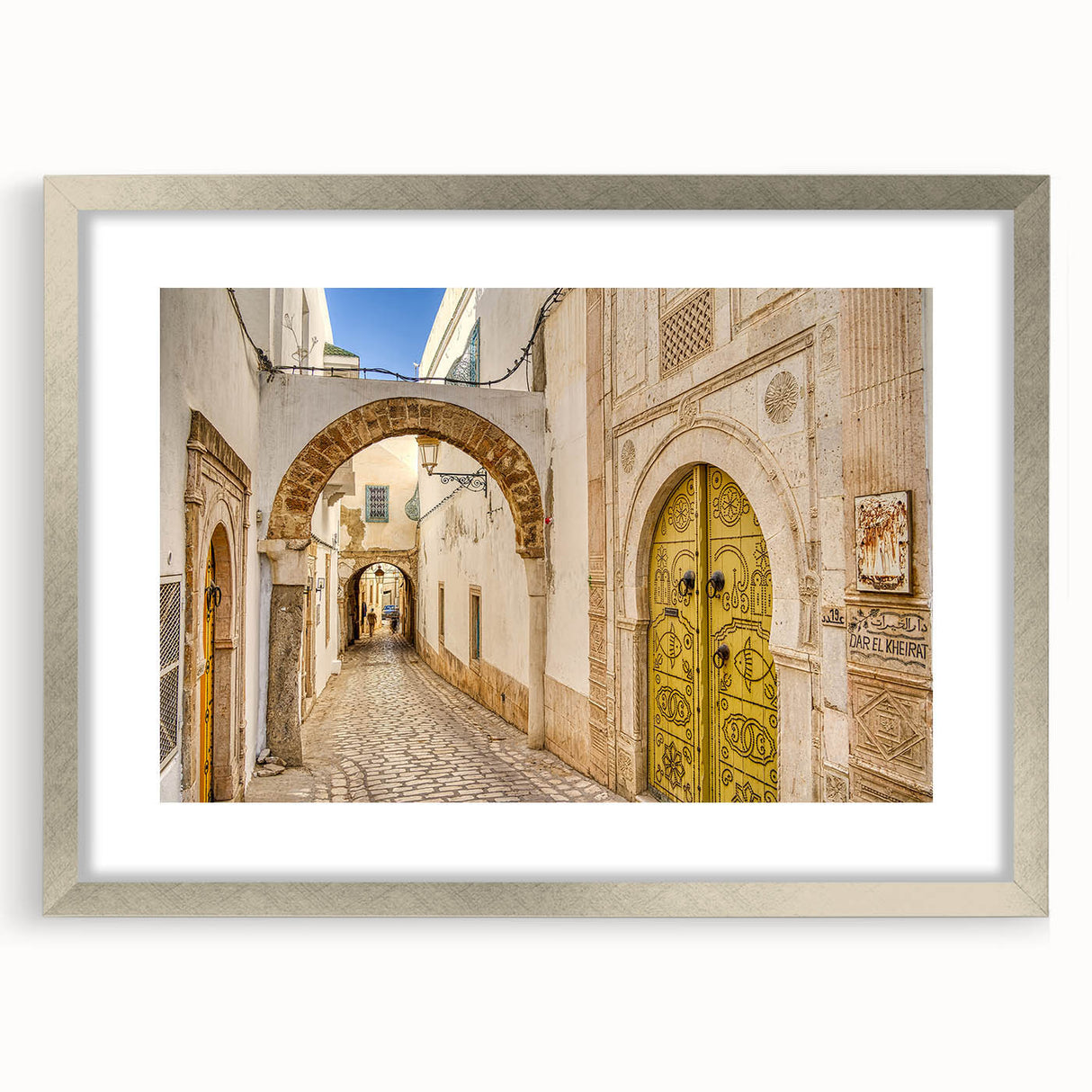 Textured abstract art print of a Tunisian landscape in earth tones on a silver-framed canvas, suitable for bedroom decor.