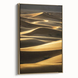 Framed canvas artwork showcasing a serene landscape of rolling sand dunes in soft beige and gold tones, presented from a side view to highlight its elegant frame and textures.