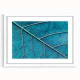 Abstract art print of close-up leaves in muted green and brown tones, framed in white, suitable for dining room decor.