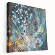 Abstract splatter artwork on stretched canvas showcasing vibrant colors like blue, orange, and yellow. This side view highlights the textured surface and gallery wrap, perfect for modern home decor.