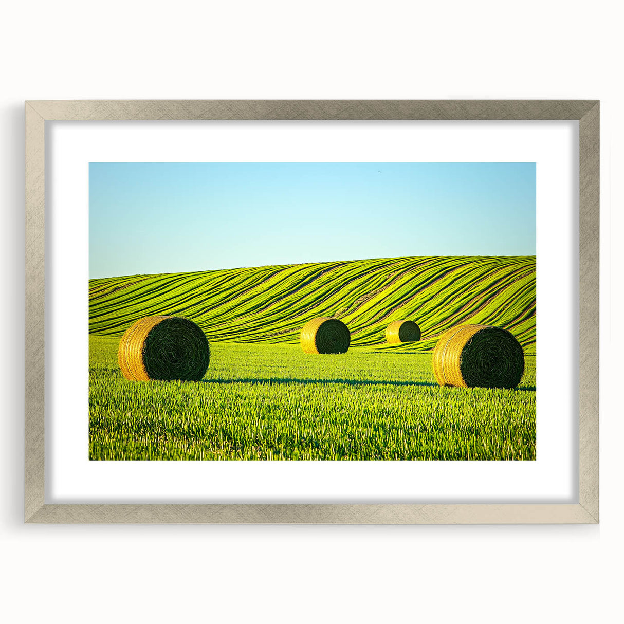 Framed landscape art print featuring vibrant green fields under a clear blue sky, elegantly displayed in a silver mat frame, perfect for home decor.