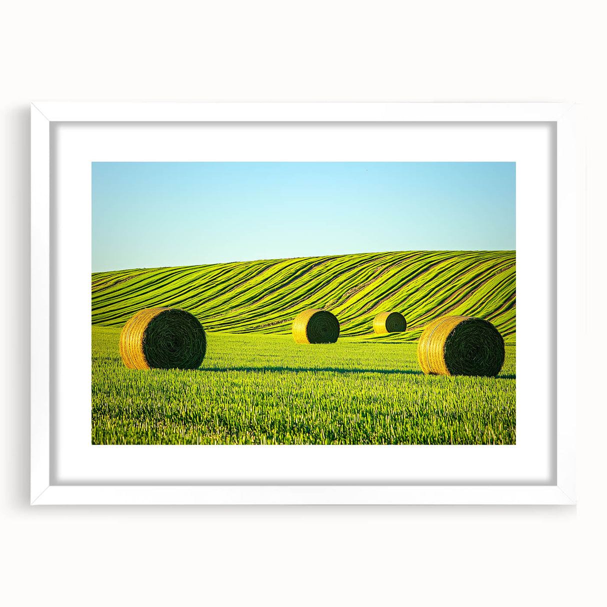 White framed landscape artwork featuring vibrant green fields and a serene blue sky, designed with a mat for an elegant presentation, perfect for home décor.