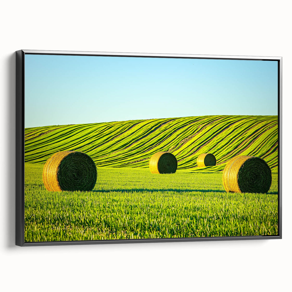 Framed canvas artwork showcasing a serene landscape of rolling fields in vibrant greens and yellows, presented in a sleek black frame, perfect for home decor.