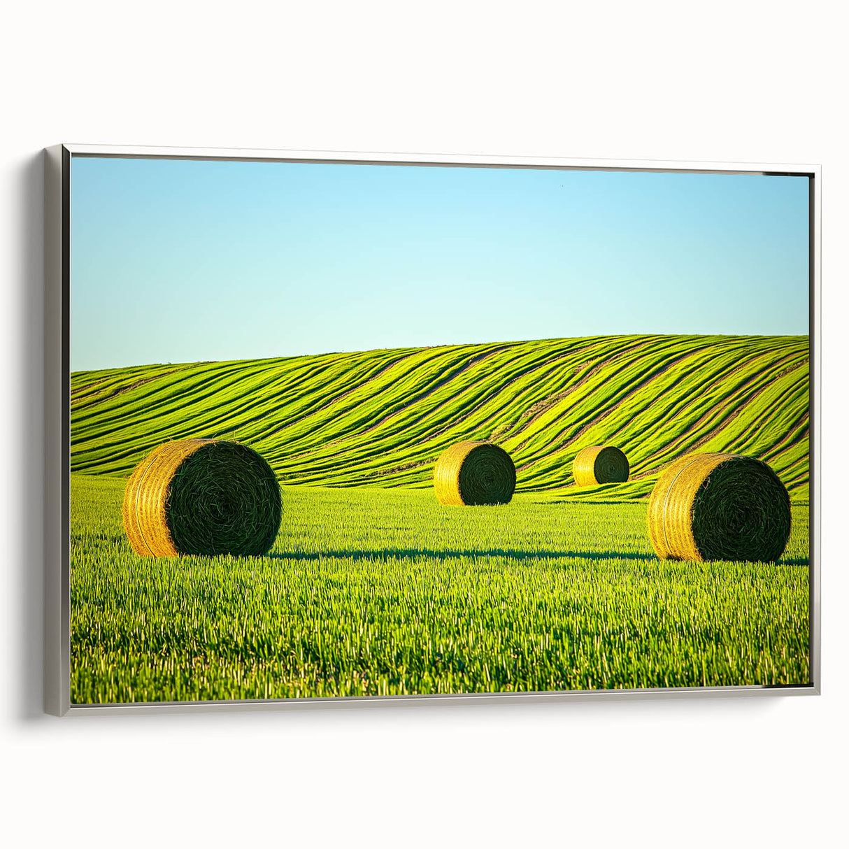 Framed canvas artwork of a serene landscape featuring lush green fields and a clear blue sky, presented in a sleek silver frame, ideal for home decor enhancement.