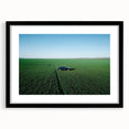 Black-framed landscape art print showcasing a serene countryside scene with vibrant greens and rolling hills, enhanced by a white mat, perfect for home decor.