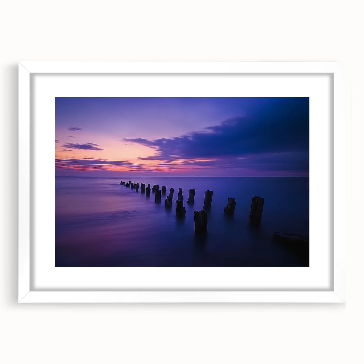 Framed landscape artwork depicting a serene beach scene with soft waves and a clear blue sky, set in a sleek white mat for an elegant presentation.