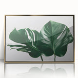 Framed wall art featuring a vibrant monstera plant design with botanical elements, set in an elegant gold frame, ideal for modern home decor.