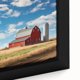 Close-up of a framed canvas wall art piece depicting a picturesque landscape with rustic barns and vibrant, lush greenery, ideal for home decor.