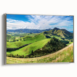 Framed canvas wall art showcasing a serene countryside landscape with vibrant greens and blues, accented by a sleek silver frame, ideal for home decor.