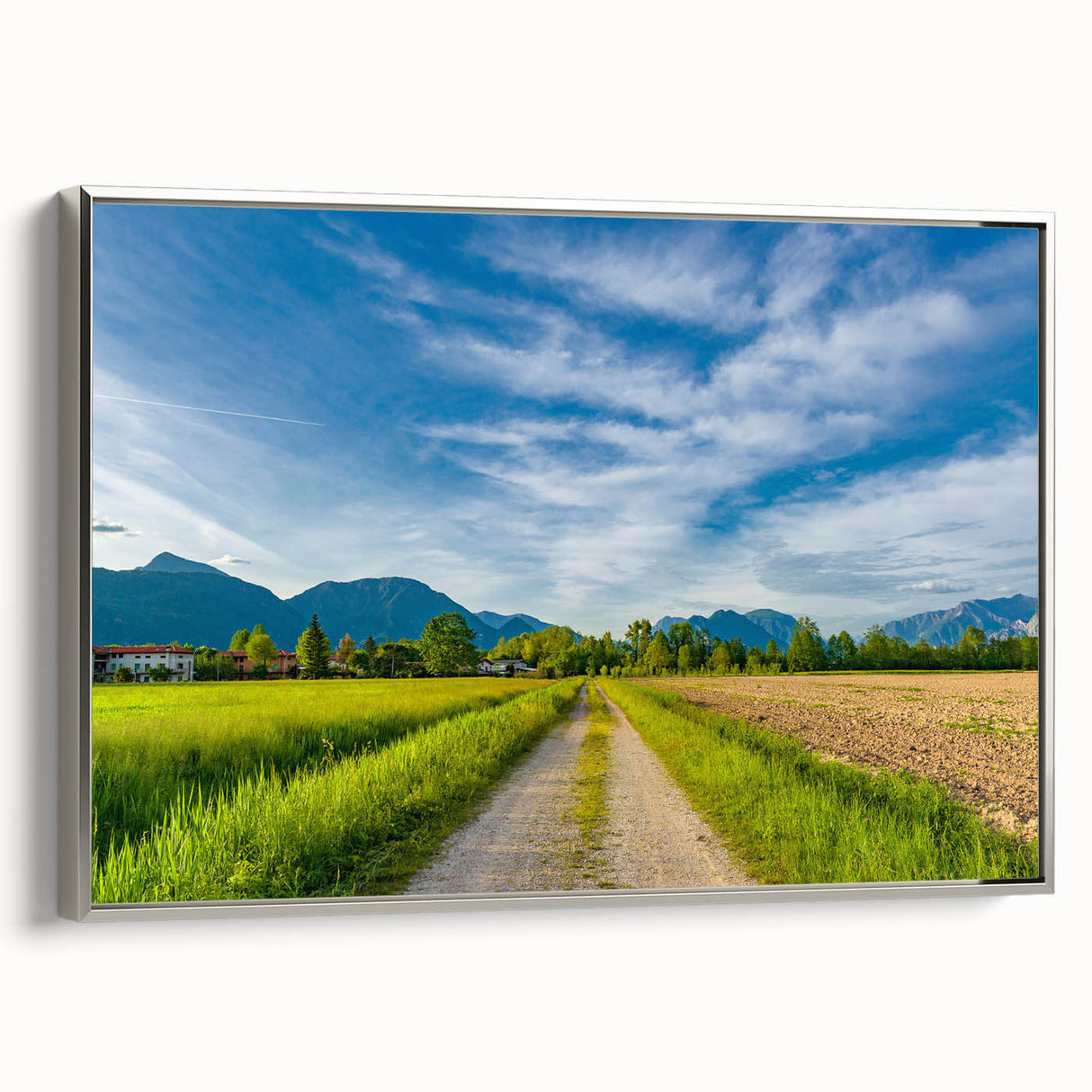 Framed canvas wall art depicting a serene countryside landscape, featuring lush green fields and distant mountains, presented in a sleek silver frame for a modern touch.