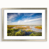 Framed wall art design showcasing a serene marsh landscape with vibrant greens and soft blues, featuring a sleek silver frame and white matting, perfect for home decor.