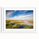 Framed wall art featuring a serene marsh landscape with vibrant greens and blues, complemented by a white mat, creating a calming focal point for home decor.