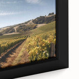 Close-up of a framed canvas wall art piece showcasing a vibrant vineyard landscape, featuring lush green grapevines and rolling hills under a bright blue sky, perfect for home decor.