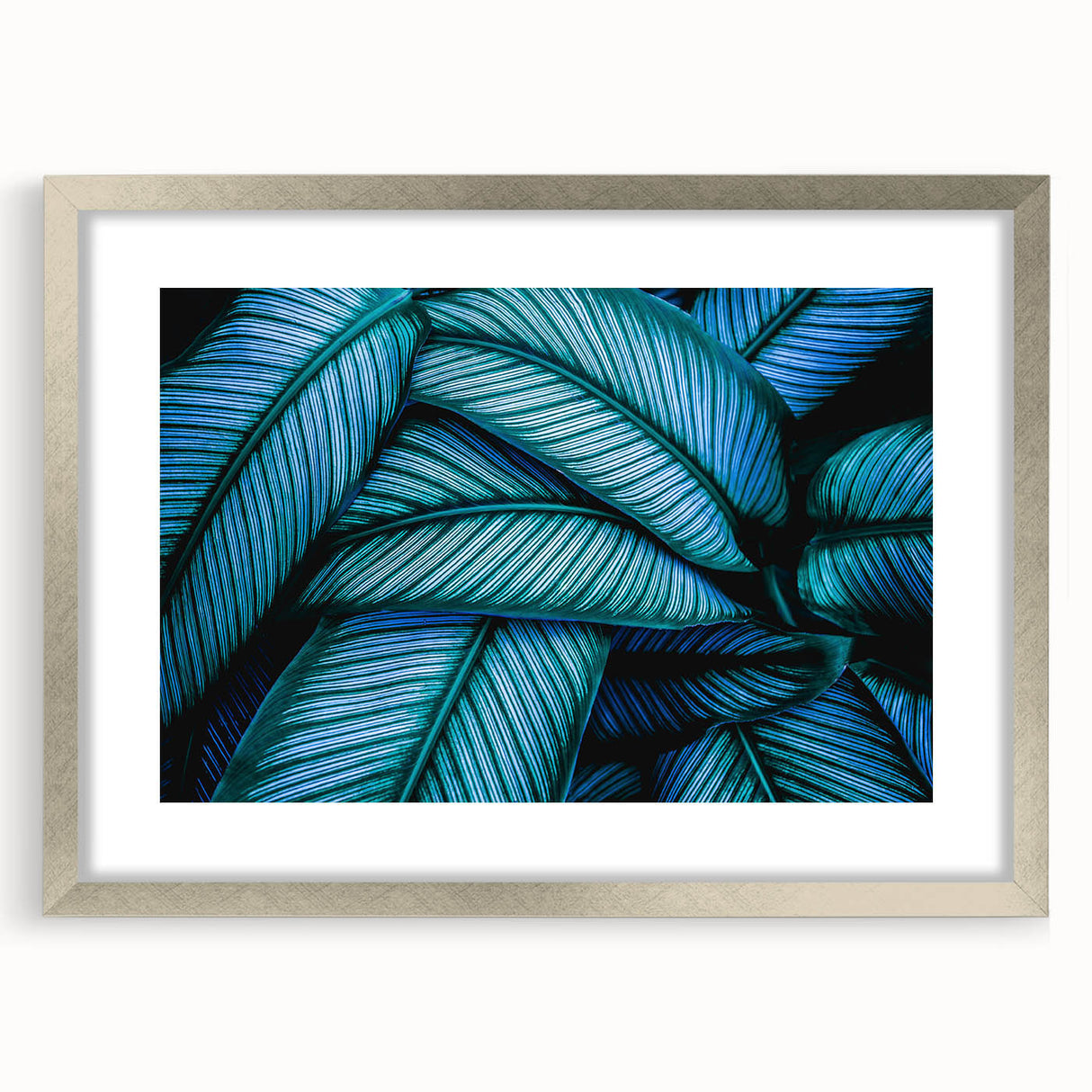 Close-up of textured art featuring abstract leaf designs in muted green and brown tones on a silver-framed mat.