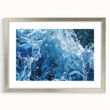 Textured abstract art print featuring rippling water designs in muted blue and gray, framed in silver.